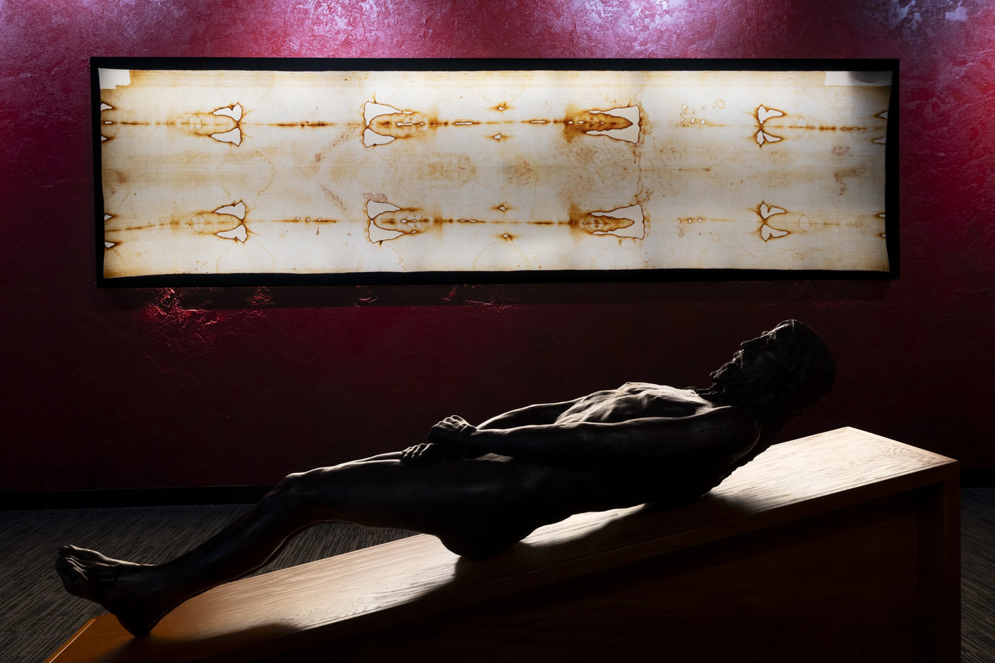 Silhouette of a bronze statue lying on a wooden platform with a framed image of the Shroud of Turin above. Located in Garden Grove.