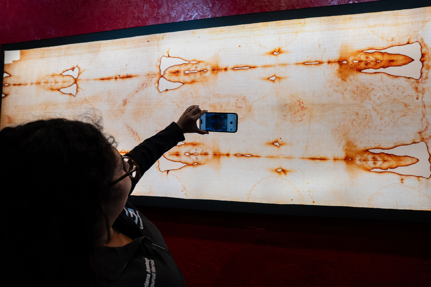 Person taking a photo of the Shroud of Turin replica with a smartphone.
